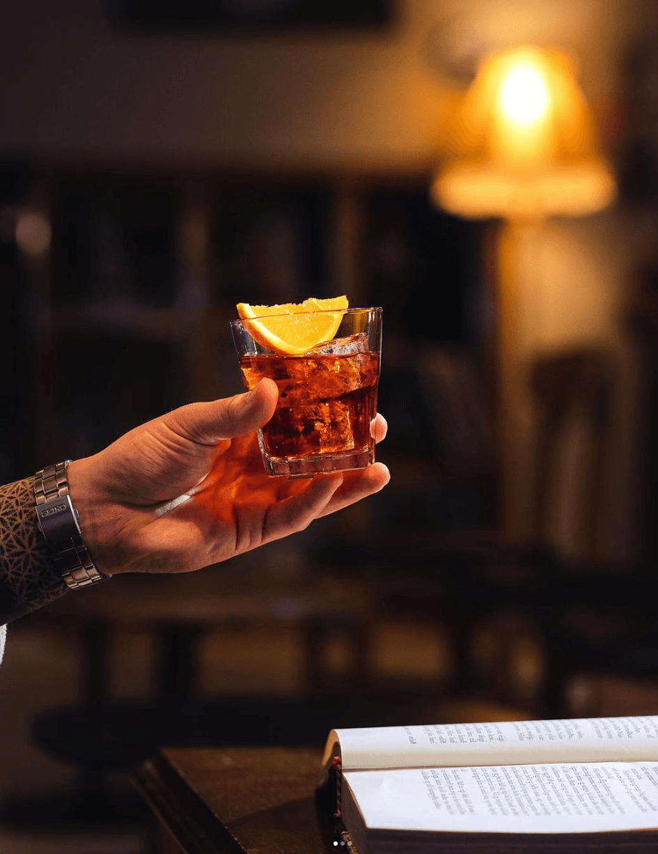 Hönd heldur á kokteil við hlið bókar